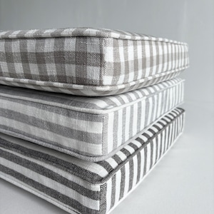 May include: Three stacked square cushions with gray and white patterns. The top cushion has a gingham pattern, the middle one has vertical stripes, and the bottom one has wider vertical stripes. All have a gray border.