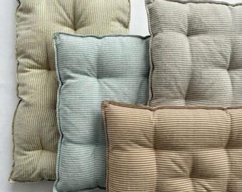 May include: A collection of tufted linen cushions in various sizes and colors, including beige, light blue, and brown, with a striped pattern. The text "PURE LINEN" is visible in green. These cushions are suitable for home decor.