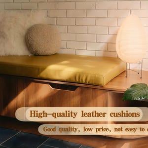 May include: A mustard-yellow leather cushion sits atop a wooden bench, complemented by a fluffy white pillow and a round, textured beige cushion. A paper lantern lamp and greenery are also visible.