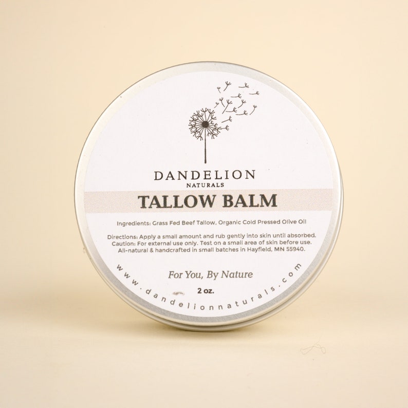 May include: A round, silver-colored tin of Dandelion Naturals Tallow Balm. The label features the text "TALLOW BALM" and a dandelion illustration. The tin contains 2 oz of balm and is made with natural ingredients.