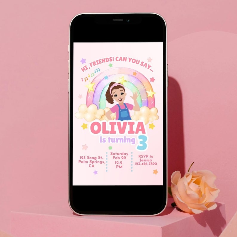 May include: A smartphone displays a birthday invitation. The invitation features a cartoon girl, a rainbow, and the text "OLIVIA is turning 3." Additional text includes date, time, address, and RSVP information. The phone rests on a pink surface.