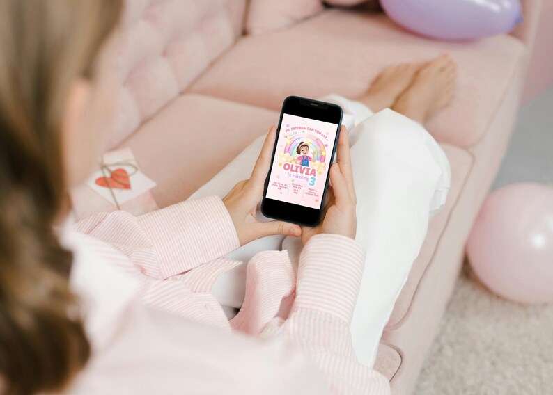 May include: A smartphone displays a birthday invitation with a rainbow, a girl illustration, and the name "Olivia." The invitation includes the number "3" and other event details. The phone is held by a person wearing a pink striped shirt.