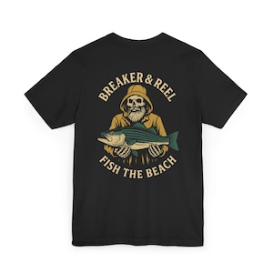 May include: Black t-shirt featuring a graphic of a bearded fisherman holding a striped fish. The design includes the text "BREAKER & REEL" above the fisherman and "FISH THE BEACH" below.