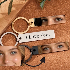 Puede incluir: Llaveros con etiquetas metálicas rectangulares que muestran imágenes de ojos y el texto "I Love You". Un llavero tiene un anillo dorado, otro plateado y el tercero negro. El fondo es un corcho.