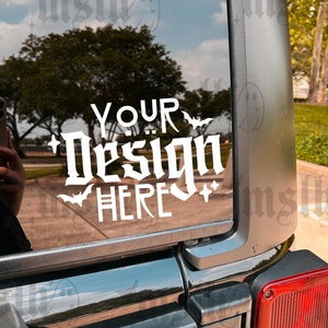 May include: A black car with a white vinyl decal on the back window. The decal says "YOUR DESIGN HERE" in a gothic font with bats and stars around the text.
