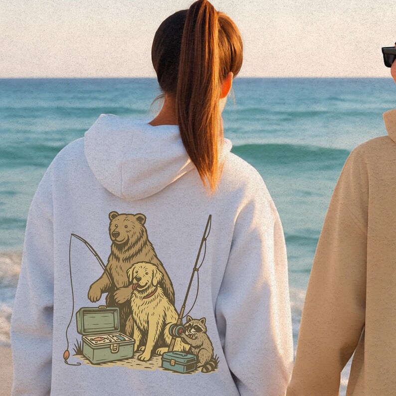 Peut inclure: Un sweat &agrave; capuche gris clair avec un motif d'ours, de chien et de raton laveur p&ecirc;chant. L'illustration comprend des cannes &agrave; p&ecirc;che, des bo&icirc;tes &agrave; p&ecirc;che et une sc&egrave;ne de plage. Le sweat &agrave; capuche a une capuche et est fait d'une mati&egrave;re douce.