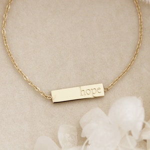 May include: A gold chain bracelet with a small rectangular charm that says "hope" on it.