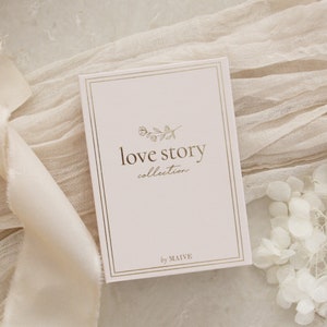 May include: A white card with a gold border and gold lettering. The card says "love story collection" with a small floral design above the text. The text "by MAIVE" is at the bottom of the card.
