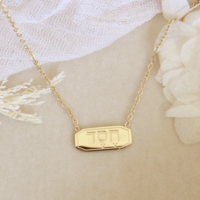 May include: A gold necklace with a rectangular pendant that says "TOD" in Hebrew letters.