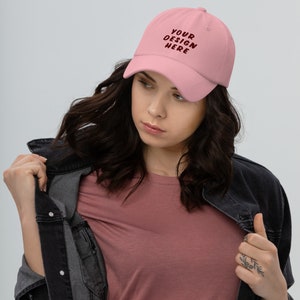 May include: A pink baseball cap with the text "YOUR DESIGN HERE" embroidered in maroon.