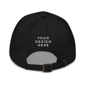 May include: Black baseball cap with an adjustable strap and the text "YOUR DESIGN HERE" embroidered in white on the back.