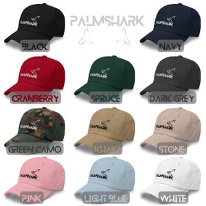 May include: A set of 12 baseball caps in various colors, including black, navy, cranberry, spruce, dark grey, green camo, khaki, stone, pink, light blue, and white. Each cap features a white embroidered shark logo with the text "PALMSHARK" underneath.