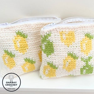 May include: Two cream-coloured crochet zipper pouches featuring a repeating pineapple design in yellow and green. The pouches have white zips and are labelled "OAKBAY CROCHET (KNIT)" and "SINCE 2016".