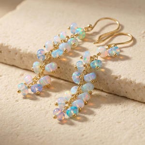 May include: Gold-tone earrings featuring a cascade of opalescent beads in shades of white, blue, and pink. The earrings have a delicate, dangling design with small gold accents, creating a sophisticated and elegant look. These earrings are perfect for adding a touch of glamour.