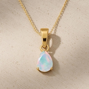 May include: A gold-colored necklace with a pear-shaped opal pendant. The opal has a mix of pastel colors, including pink, blue, and white. The pendant is held by a gold setting and hangs from a delicate gold chain.