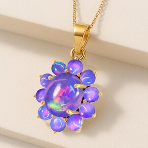May include: A gold-colored necklace featuring a pendant with a large, oval, iridescent purple gemstone surrounded by smaller, round, purple gemstones. The pendant is suspended from a delicate gold chain.