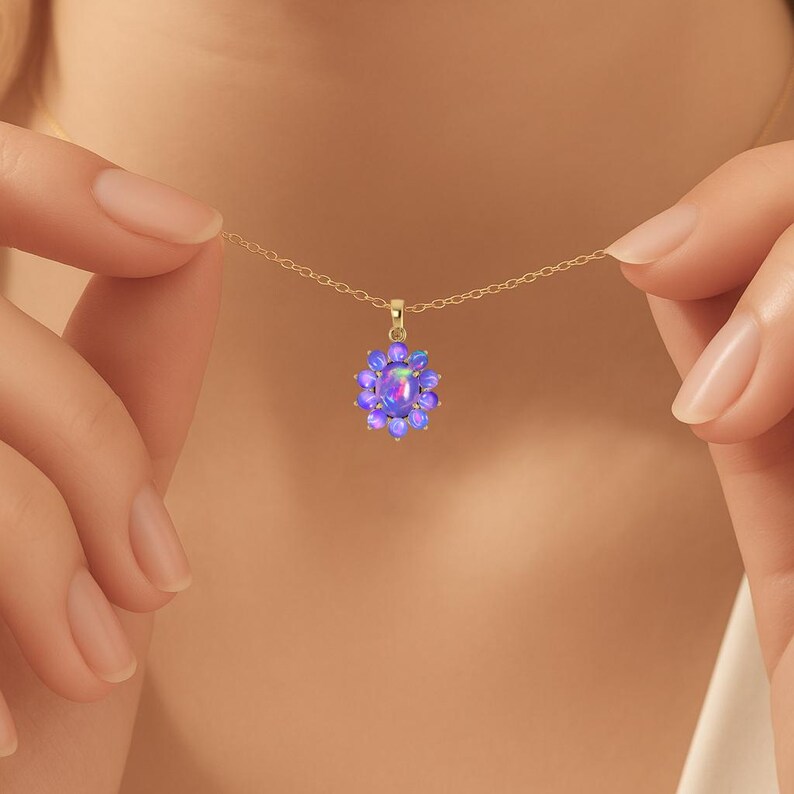 May include: A gold necklace with a pendant featuring a cluster of purple opals. The pendant is in the shape of a flower, with a central opal surrounded by smaller opals. The necklace is held by a person.