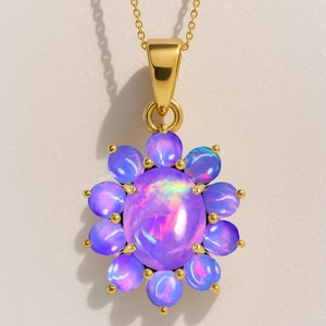 May include: A gold-toned necklace featuring a pendant with a large, oval, iridescent opal stone at the center, surrounded by smaller, round, purple-blue opals. The pendant is flower-shaped and hangs from a delicate chain.