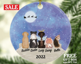 May include: A round, white ceramic ornament with a blue starry night sky background. Five dogs are silhouetted against the moon, with names "Buddie, Sadie, Lucy, Daisy, Bella" and the year "2022" printed below.