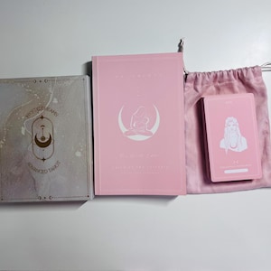 May include: A tarot set comprising a box, a book, a deck of cards, and a drawstring bag. The box is grey with gold and white accents and the words "Mystic Dreams Advanced Tarot". The book and cards are pink with white illustrations.