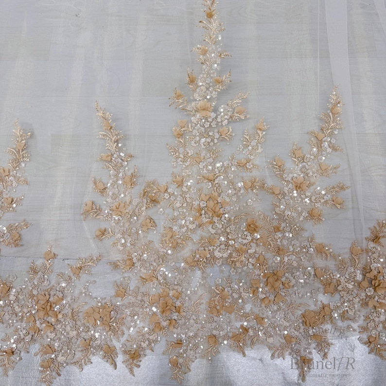K&ouml;nnte beinhalten: Ein transparenter wei&szlig;er T&uuml;llstoff mit aufwendigen Stickereien in Beige- und Champagnert&ouml;nen. Das Design umfasst dreidimensionale florale Applikationen, zarte Blattmuster und verstreute klare Pailletten, die f&uuml;r einen dezenten Glanz sorgen.