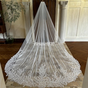 Peut inclure: Un long voile de mariée blanc avec une bordure en dentelle florale délicate. Le voile est en tulle doux et a une longueur cathédrale.