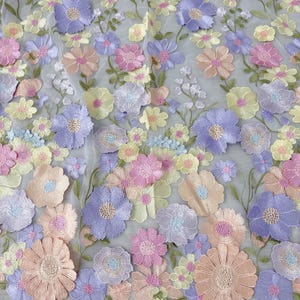 May include: A close-up of a floral fabric with embroidered flowers in pastel colors. The flowers are in shades of pink, purple, yellow, and peach, with green stems and leaves. The fabric has a sheer, light gray background.