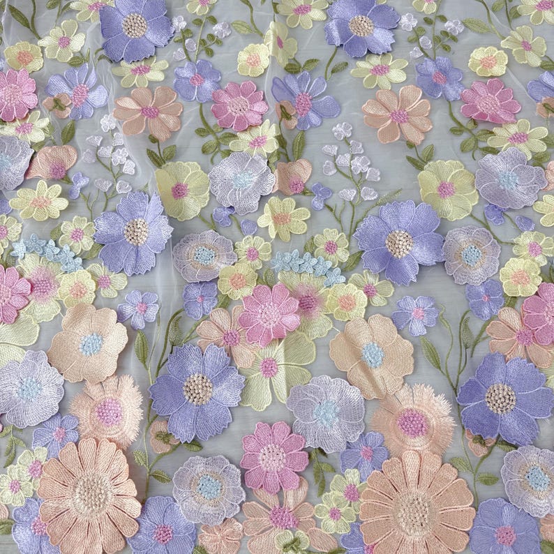 May include: A close-up of a floral fabric with embroidered flowers in pastel colors. The flowers are in shades of pink, purple, yellow, and peach, with green stems and leaves. The fabric has a sheer, light gray background.