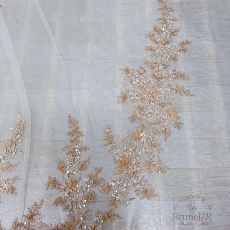 K&ouml;nnte beinhalten: Ein transparenter wei&szlig;er T&uuml;llstoff mit aufwendigen Stickereien in Beige- und Cremet&ouml;nen. Das Design umfasst florale Motive, kleine Stoffbl&uuml;tenbl&auml;tter und verstreute klare Pailletten, die einen strukturierten und schimmernden Effekt erzeugen.