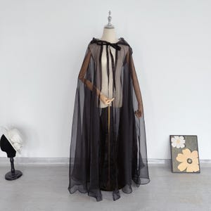 Peut inclure: Une cape noire en voile avec une capuche et un ruban noir. La cape est drapé sur un mannequin.