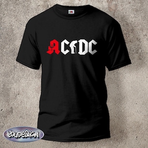 May include: A black short-sleeve t-shirt featuring a graphic print on the chest. The design displays the text ACDC in a bold font, where the letter A is red and the remaining letters are white. A silhouette of an elderly person with a cane replaces the letter C.