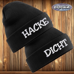 Könnte beinhalten: Zwei schwarze Mützen mit weiß gesticktem Text. Auf der oberen Mütze steht "HACKE" und auf der unteren Mütze steht "DICHT". Die Mützen werden vor einem Holz Hintergrund gezeigt.