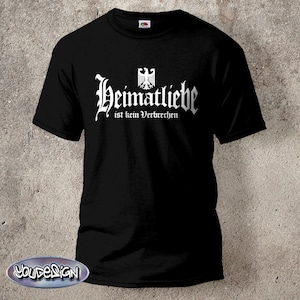 Op de afbeelding: Een zwart T-shirt met korte mouwen en witte tekst die Heimatliebe ist kein Verbrechen leest in een gotisch lettertype. Boven de tekst staat een wit grafisch symbool van een gestileerde adelaar. Het shirt heeft een ronde hals en een standaard pasvorm.