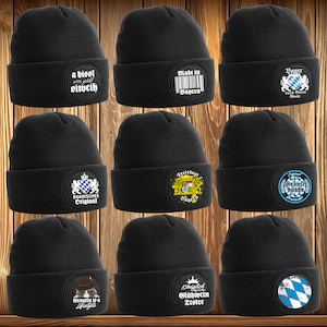 Könnte beinhalten: Zehn schwarze Strickmützen mit verschiedenen gestickten Aufnähern. Die Aufnäher zeigen bayerische Symbole, Texte und Bilder. Die Mützen sind alle schwarz und haben eine gerippte Struktur.
