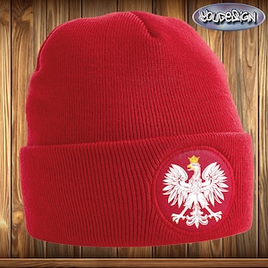 Op de afbeelding: Rode gebreide beanie met een wit geborduurd Pools adelaarsembleem op de voorkant.