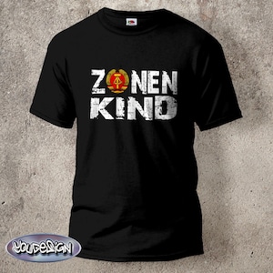 Könnte beinhalten: Schwarzes T-Shirt mit weißem Text "ZONEN KIND" und einem roten und goldenen Emblem.