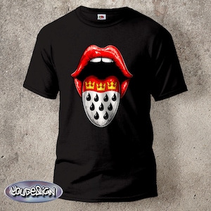 Puede incluir: Camiseta negra con un gráfico de labios rojos y una lengua que muestra el escudo de armas de Colonia, Alemania. La lengua tiene tres coronas doradas y formas de lágrima negras. La camiseta tiene cuello redondo.
