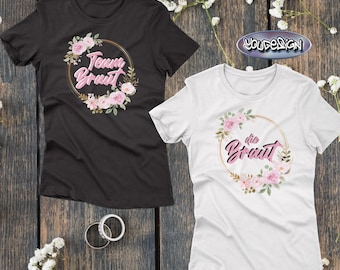 May include: Black and white t-shirts with floral designs. The black shirt has the text "Team Braut" inside a gold circle with pink flowers. The white shirt has the text "die Braut" inside a gold circle with pink flowers.