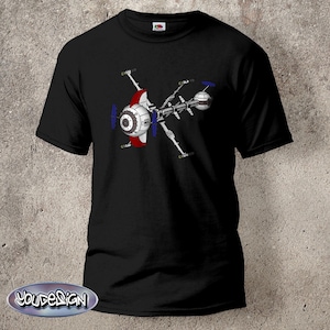 May include: Black t-shirt with a graphic of a futuristic spaceship in white, red, and blue. The design shows detailed mechanical elements and a central circular component. The shirt has a crew neck and short sleeves.