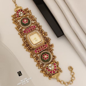 Op de afbeelding: Een sierlijk goudkleurig erfgoedhorloge met een vierkante wijzerplaat en een crèmekleurige wijzerplaat. Het horloge heeft ingewikkelde details met rode en groene accenten en een armband met schakels. De tekst "No.-235. HERITAGE WATCH D:4-St" is zichtbaar.