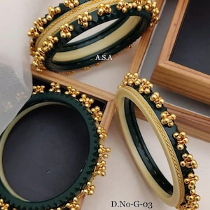 May include: Set of four green and white bangles with gold accents. The bangles are decorated with small gold balls and have a chain-like design. The bangles are labeled "D.No-G-03 4. Pic Ghughari Bangals Size. 2/4. 2/6. 2/8. 2/10 No.25"