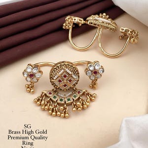 May include: Two gold-toned brass double-finger rings featuring intricate metalwork, small white pearls, and inlaid red and green stones. The rings have dangling metal beads and floral accents. Text on the image reads: SG Brass High Gold Premium Quality Ring No.72.