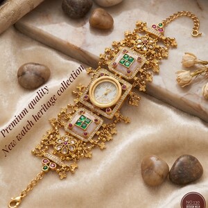 May include: Gold-toned watch with a white face and ornate detailing. The watch features square and circular frames with red and green gemstones. The text "Premium quality New watch heritage collection" is visible.