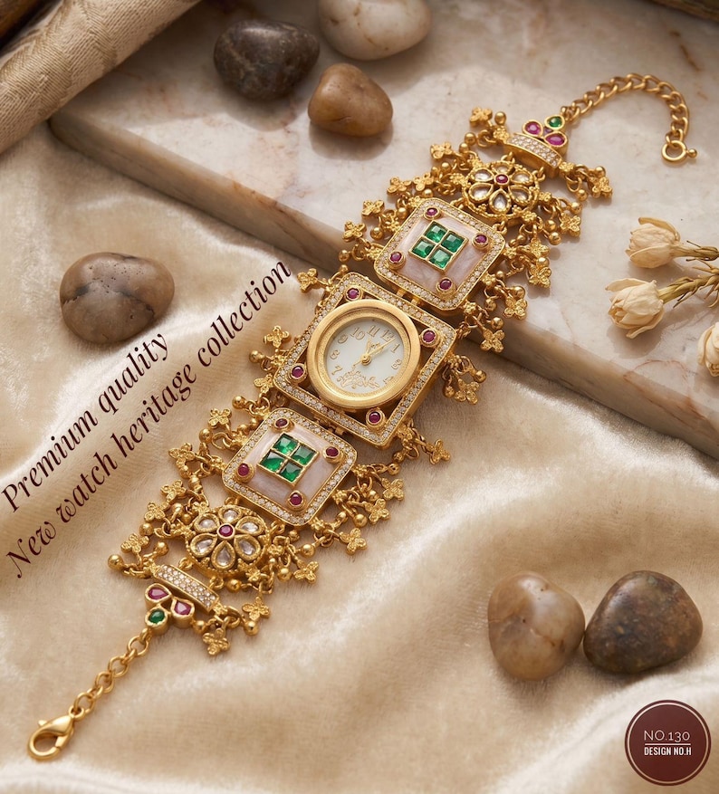 May include: Gold-toned watch with a white face and ornate detailing. The watch features square and circular frames with red and green gemstones. The text "Premium quality New watch heritage collection" is visible.