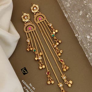May include: Gold-toned Kashmiri earrings with floral and half-moon designs. The earrings feature dangling chains with small beads and colorful accents of pink, green, and white. The text on the image reads "Kashmiri Earrings".