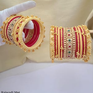 Può includere: Un set di braccialetti rossi e avorio con accenti dorati e decorazioni. I braccialetti sono decorati con piccole perline e disegni intricati. Rajwadi Met Chudla set S.105