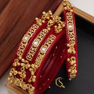 May include: Set of five red bangles with gold accents and clear stones. The bangles are decorated with intricate designs and have a dangling charm. The bangles are labeled "No:-35. 4-pice Bengal's 2.2/2.4/2.6/2.8/2.10/"