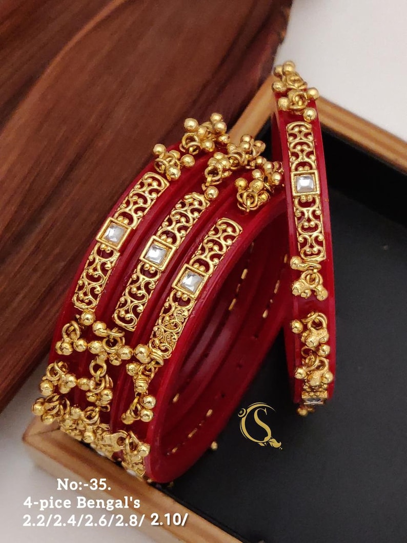May include: Set of five red bangles with gold accents and clear stones. The bangles are decorated with intricate designs and have a dangling charm. The bangles are labeled "No:-35. 4-pice Bengal's 2.2/2.4/2.6/2.8/2.10/"