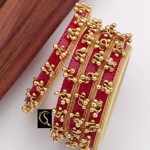 Puede incluir: Conjunto de cuatro pulseras rojas y doradas con un diseño de cuentas. Las pulseras tienen un diámetro de 5,6, 6,1, 6,6 y 7,1 cm.