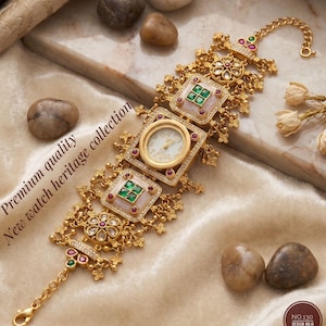 May include: Gold-toned watch with a white face and ornate detailing. The watch features square and circular frames with red and green gemstones. The text "Premium quality New watch heritage collection" is visible.